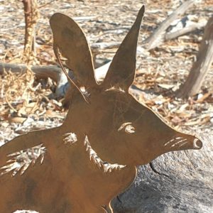 A handmade Bilby standing garden stake made from Corten steel, measuring 27 cm, showcasing its charming long-nosed design in an outdoor garden setting
